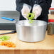 A person pouring celery and carrots into a Vollrath Wear-Ever sauce pan with a blue silicone handle.