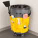 A yellow Continental caddy bag on a Huskee trash can filled with cleaning supplies including a broom and spray bottle.