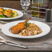 A Libbey Porcelana white porcelain plate with food on a table.