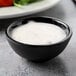 A bowl of white sauce in a Tablecraft black melamine ramekin.