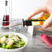 A person pouring oil into a bowl of salad.