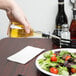 A hand pouring oil from a Tablecraft Siena oil and vinegar bottle onto a salad.