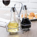 A Tablecraft oil and vinegar cruet set on a table with yellow and clear liquid in the containers.