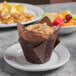 A muffin on a Libbey wide rim porcelain plate with fruit in the background.