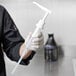 A person in a black uniform using a Carlisle condiment pump kit to fill a bottle on a counter.