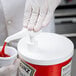 A hand using a Carlisle condiment pump to pour ketchup into a container.