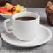 A Libbey porcelain cup of coffee on a table with a plate of fruit.