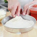 A person making pizza dough in an American Metalcraft tapered pizza pan.