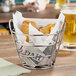 A Clipper Mill chrome plated metal round bucket basket filled with french fries on a table.