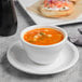 A bowl of soup on a bright white Libbey Porcelana saucer with a spoon.