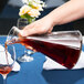 A person pouring red wine from a Stolzle Pisa carafe onto a table with a glass of red wine.