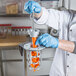 A person in a white lab coat and blue gloves using a Tellier manual upright carrot peeler.