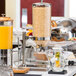 A Tablecraft stainless steel cereal dispenser on a hotel breakfast buffet table.