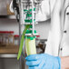 A person in a blue glove using a Tellier manual upright cucumber peeler to peel a cucumber.