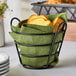 A Clipper Mill black iron wire basket with bread on a table.