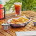 A Clipper Mill black metal wire basket with fried food and 2 ramekins on a table.