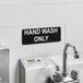 A black and white Vollrath Traex hand wash only sign on a white wall.