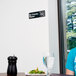 A person sitting at a table with a Vollrath No Checks Please sign next to a plate of food and a glass of water.