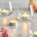 Three Leola white tea light candles burning on a table with flowers.