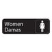 A black rectangular sign with white text that says "women" and "damas" with a white woman figure.