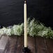 A Hyoola ivory taper candle in a white candle holder on a table.