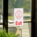 A white and red Vollrath Traex exit sign on a glass door.
