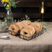 A Clipper Mill gray square wire basket filled with bagels on a table in a bakery.