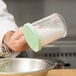 A person using a Cambro polycarbonate shaker with green lid to pour white powder into a bowl.