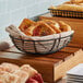 A black Clipper Mill braided wire basket of bread on a wooden counter.