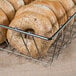 A Clipper Mill chrome-plated iron wire basket filled with bagels on a bakery counter.