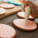 A hand using an Ateco metal circle cookie cutter to decorate a cookie with white cream.