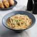 A Biseki blue stoneware coupe bowl filled with noodles in broth and vegetables.