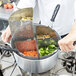 A chef using a Vollrath Wear-Ever vegetable and pasta cooker set to cook vegetables.