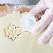 A person's hands in plastic gloves using an Ateco plastic leaf pastry cutter to cut out cookie dough.