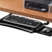 A Fellowes black underdesk keyboard drawer holding a keyboard and mouse under a desk.