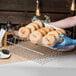 A person using a Clipper Mill clear plastic basket liner to hold a tray of bagels in a bakery display.