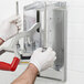 A gloved hand using a screwdriver to attach a metal Vollrath wall mount bracket to a wall.