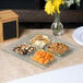 A Clipper Mill clear plastic 4-compartment tray with fruit, nuts, and crackers on a table.