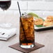 A Stolzle iced tea glass filled with brown liquid, ice, and a lime wedge.