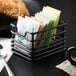 A black Clipper Mill iron sugar caddy on a counter with tea bags inside.