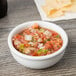 A Tuxton eggshell china bowl filled with salsa and chips on a wood table.