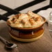 A Tuxton onion soup crock filled with French onion soup on a table.