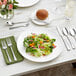 A white plate with a knife on a green napkin, next to a plate of salad.