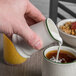 A hand pouring milk from a Tuxton Eggshell Creamer with Green Band into a cup of coffee.