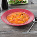 A red Tuxton china soup bowl filled with soup on a table with a salad plate.