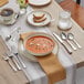 A table set with Acopa Edgeworth table knives, forks, and spoons next to a bowl of soup and a glass of water.
