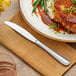 An Acopa Edgeworth stainless steel table knife on a plate of food.