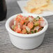 A Tuxton white porcelain ramekin filled with salsa on a wood table.