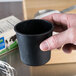 A person holding a black cup filled with white substance using a Matfer Bourgeat Rum Baba Mold.