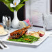 A Tuxton white square china plate with food and a glass of water on a table.